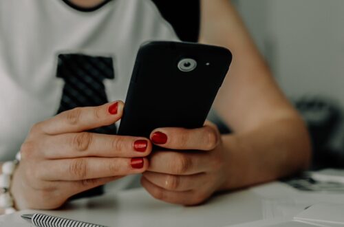 Image of a woman with red painted fingernails holding a cell phone while leaning forward onto a white desk; it's implied that she is seeking connection online with the tips from Jazmin Marie's womens travel and lifestyle blog. From Blog Post: 5 Best Online Spaces for Women to Make Friends, Find Inspiration, and Connect Virtually by Jazmin Marie - Womens Lifestyle and Travel Blog - USA Best Women's Travel Blog for Tips and Inspiration for Women Travelers -- photofromkaboompics