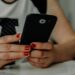 Image of a woman with red painted fingernails holding a cell phone while leaning forward onto a white desk; it's implied that she is seeking connection online with the tips from Jazmin Marie's womens travel and lifestyle blog. From Blog Post: 5 Best Online Spaces for Women to Make Friends, Find Inspiration, and Connect Virtually by Jazmin Marie - Womens Lifestyle and Travel Blog - USA Best Women's Travel Blog for Tips and Inspiration for Women Travelers -- photofromkaboompics